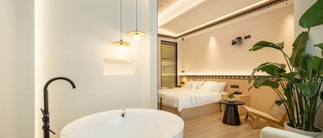 Un baño moderno con una bañera independiente, tocador y una cama en la habitación contigua.