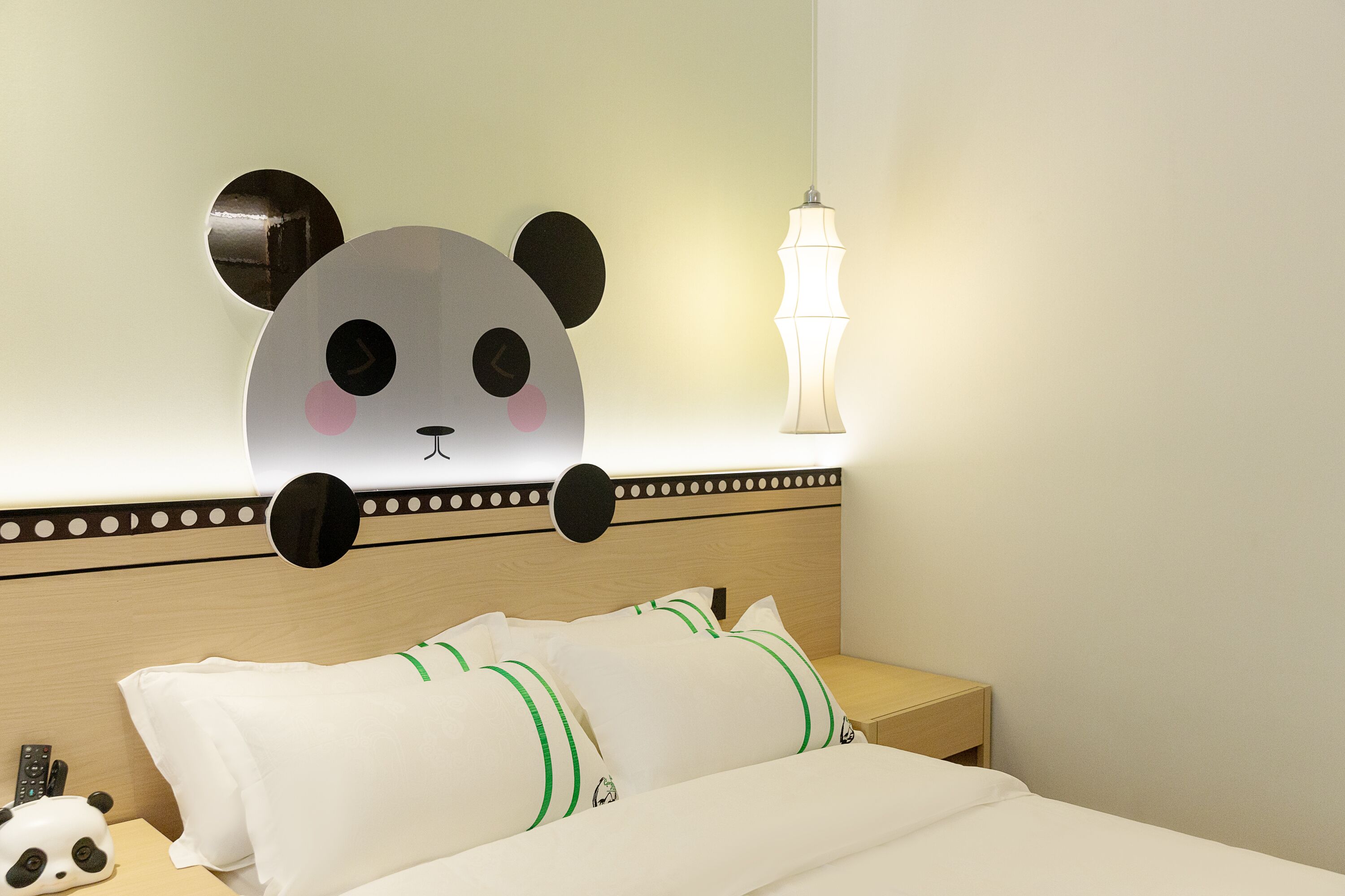 Un lit avec une literie blanche à rayures vertes, une table de chevet avec une lampe et une décoration murale représentant un panda.