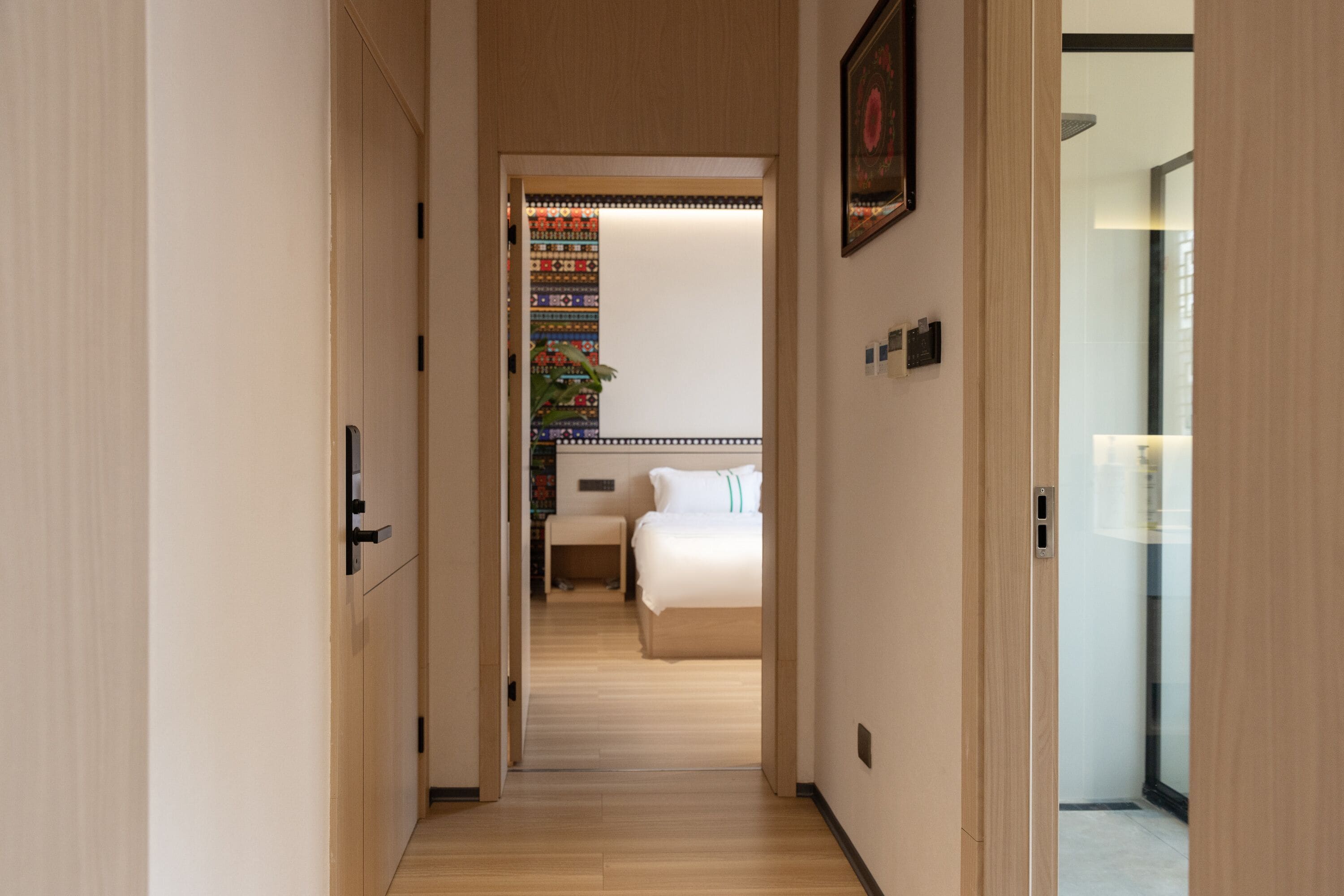 A hallway leading to a bedroom with a bed, bedside table, and a colorful wall decoration.