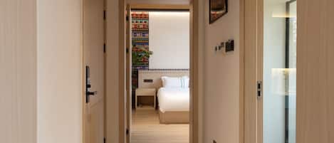 A hallway leading to a bedroom with a bed, bedside table, and a colorful wall decoration.