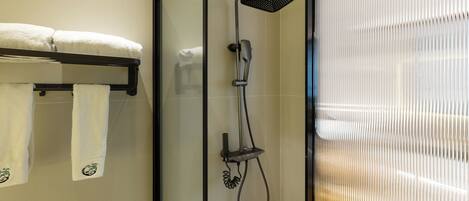 A glass-enclosed shower area with a handheld showerhead and a towel rack with two towels.