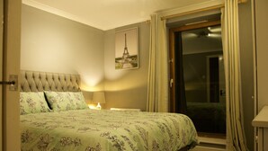 A hotel room with a bed, a nightstand, a lamp, a door leading to a balcony, and a picture of the Eiffel Tower on the wall. - Meridian Stays Canary Wharf Near O2 Arena (London)