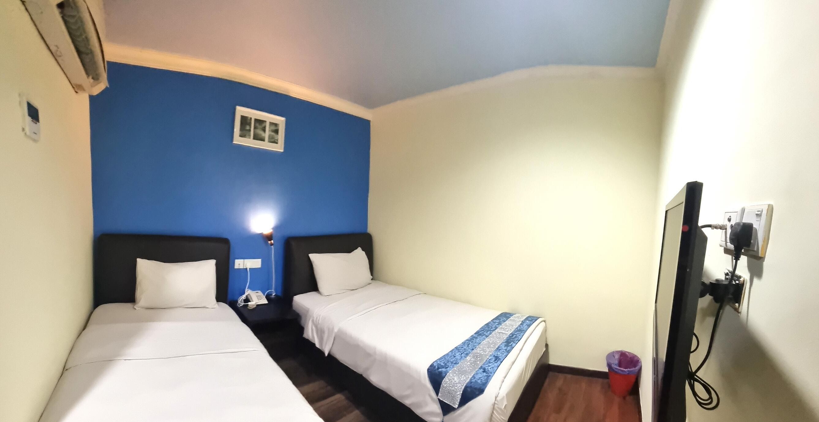 A room with two beds, a small window, a wall-mounted TV, and a power outlet.