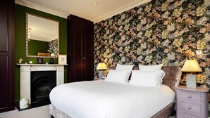 Een slaapkamer met een groot bed, een open haard, een spiegel en bloemen behang.