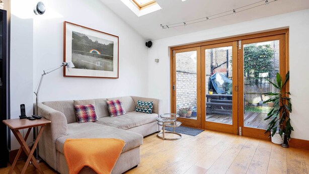 A modern living room with a sofa, a side table, a lamp, and a large window with a view of the outside. - The Tranquil Townhouse, by Veeve (London)