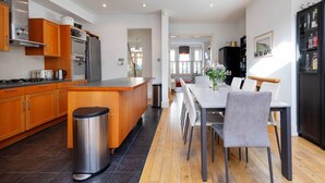A modern kitchen with wooden cabinets, stainless steel appliances, and a dining area with a table and chairs. - The Tranquil Townhouse, by Veeve (London)