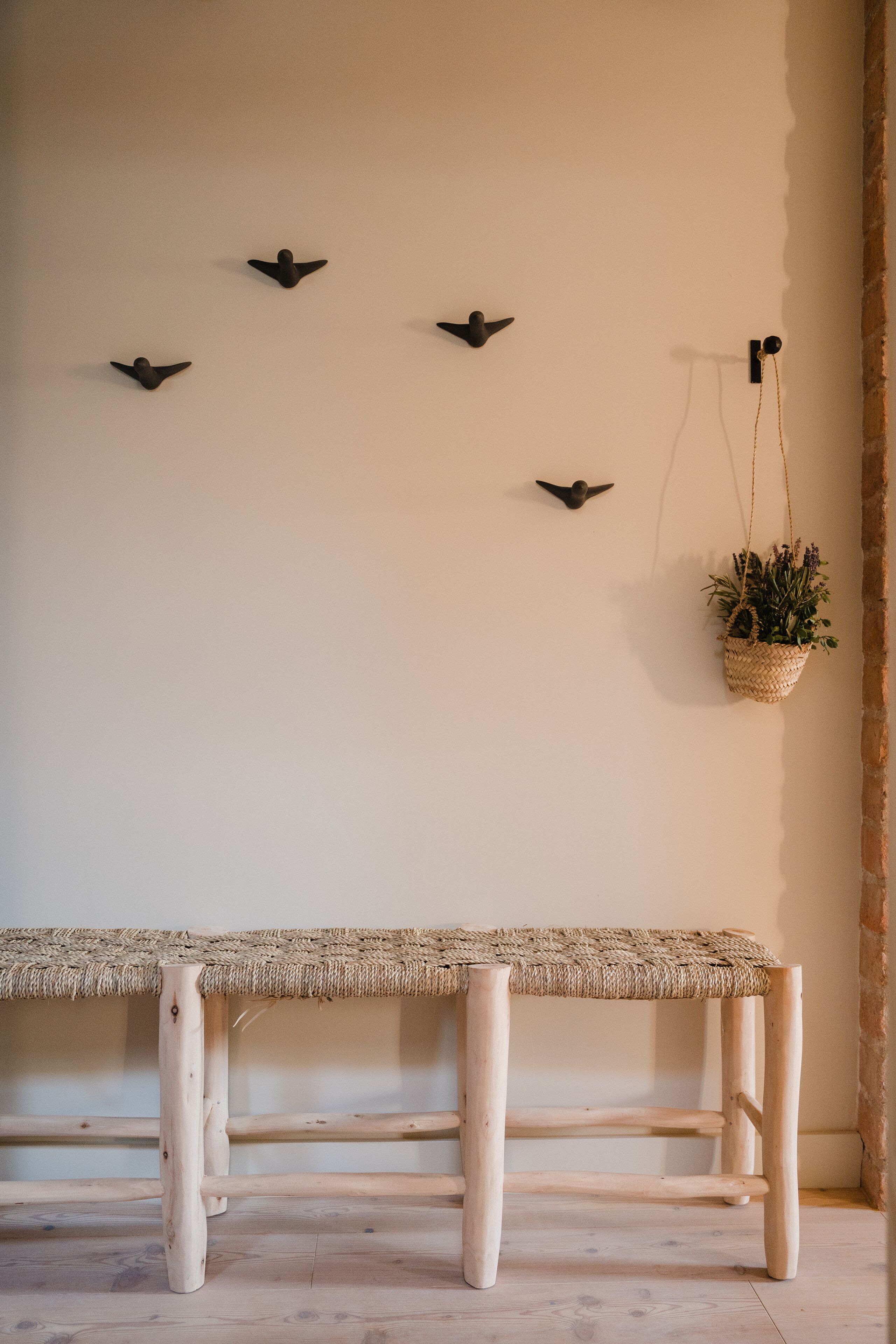 Un banc en bois rustique avec une assise en osier tressé, une plante fixée au mur et une décoration murale en forme d’oiseau.