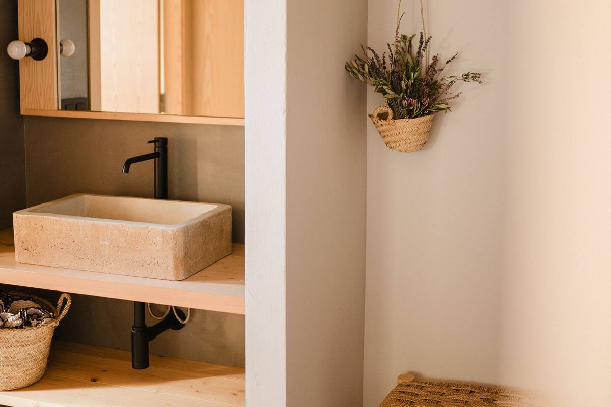 A bathroom with a wooden vanity, a large mirror, a hanging plant, and a small stool.