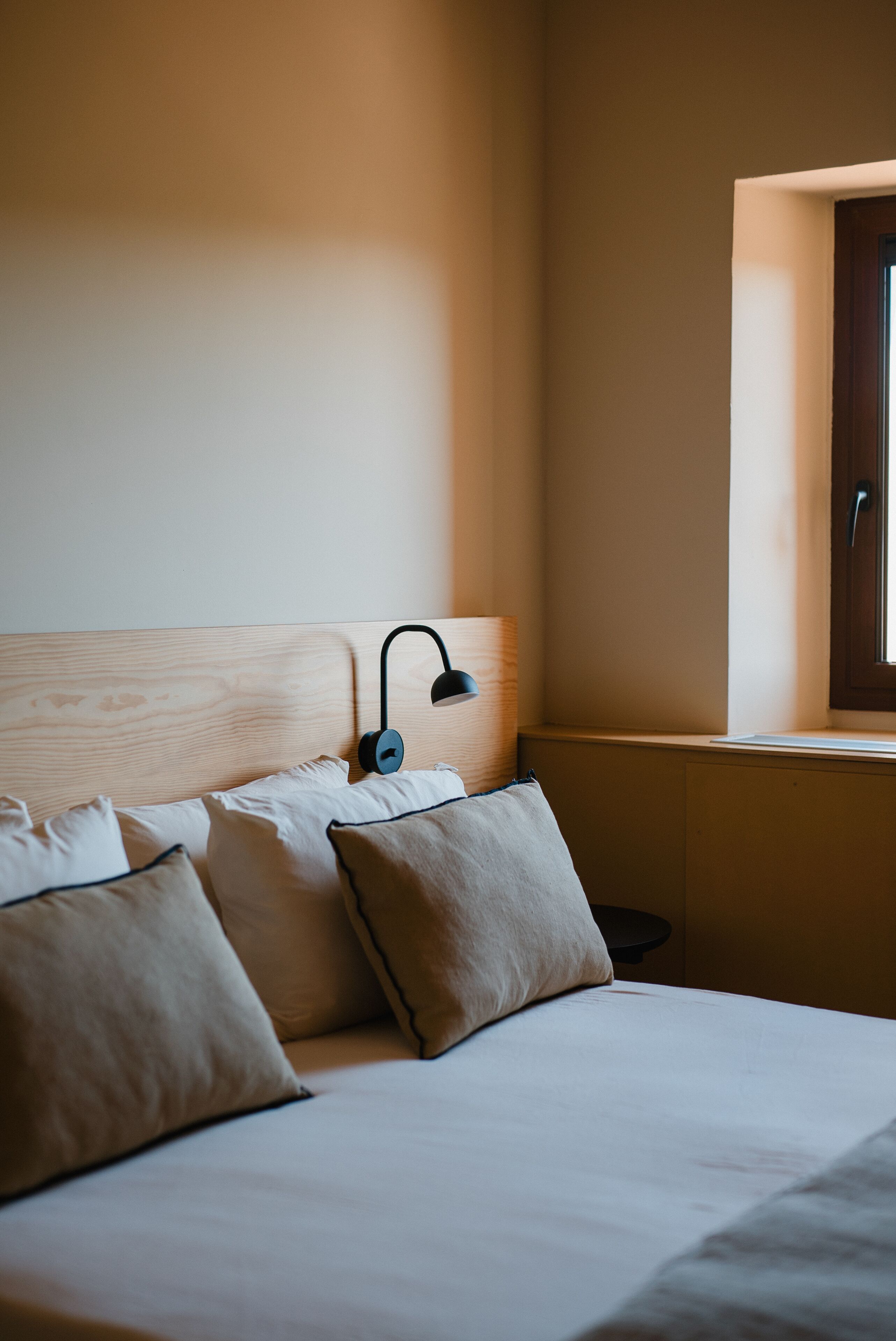 Un dormitorio con cabecera de madera, lámpara de noche y ventana con vistas al exterior.