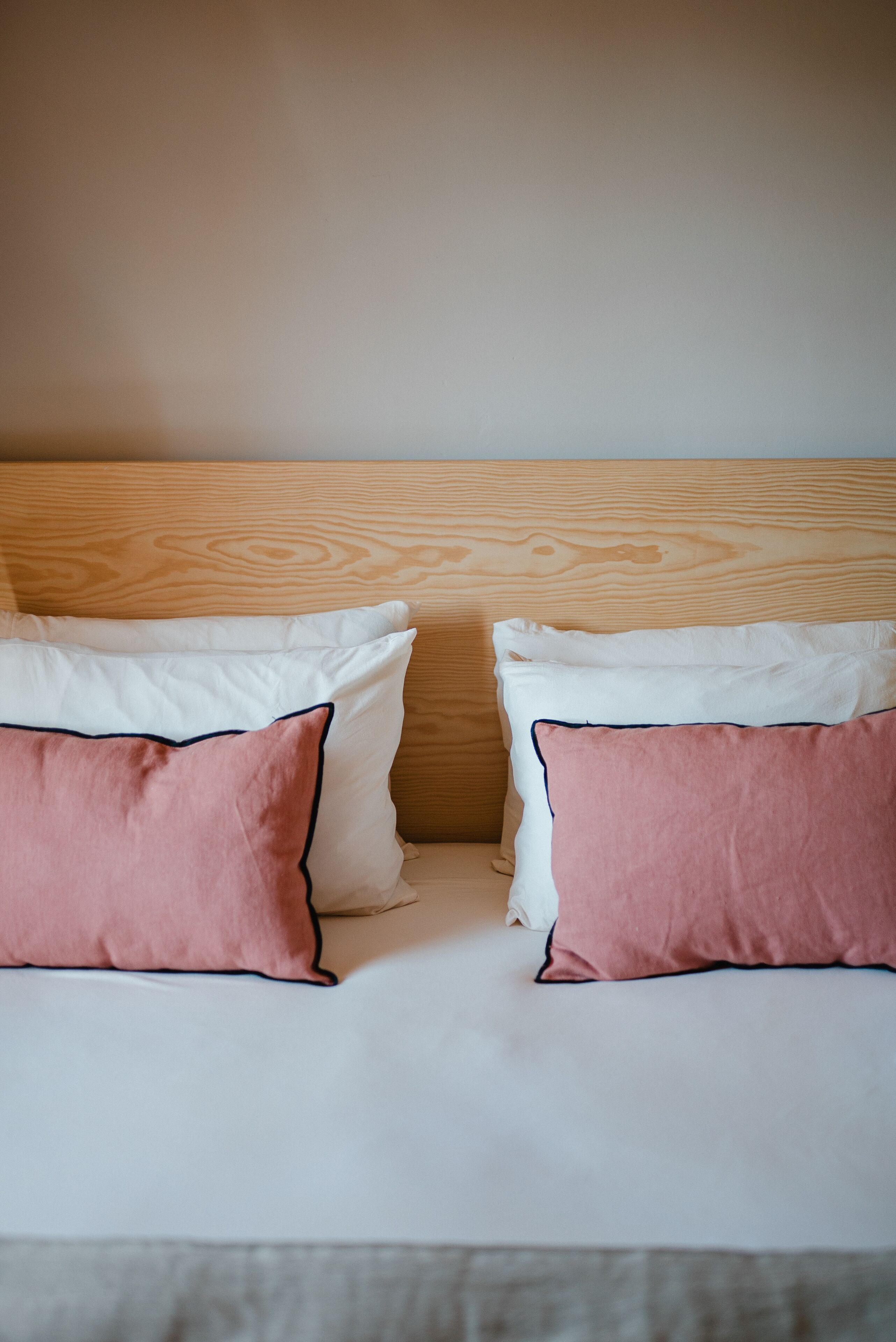 Una cama con dos almohadas, una rosa y otra blanca, y un cabecero de madera.