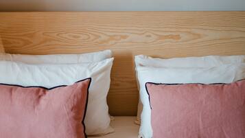 Una cama con dos almohadas, una rosa y otra blanca, y un cabecero de madera.