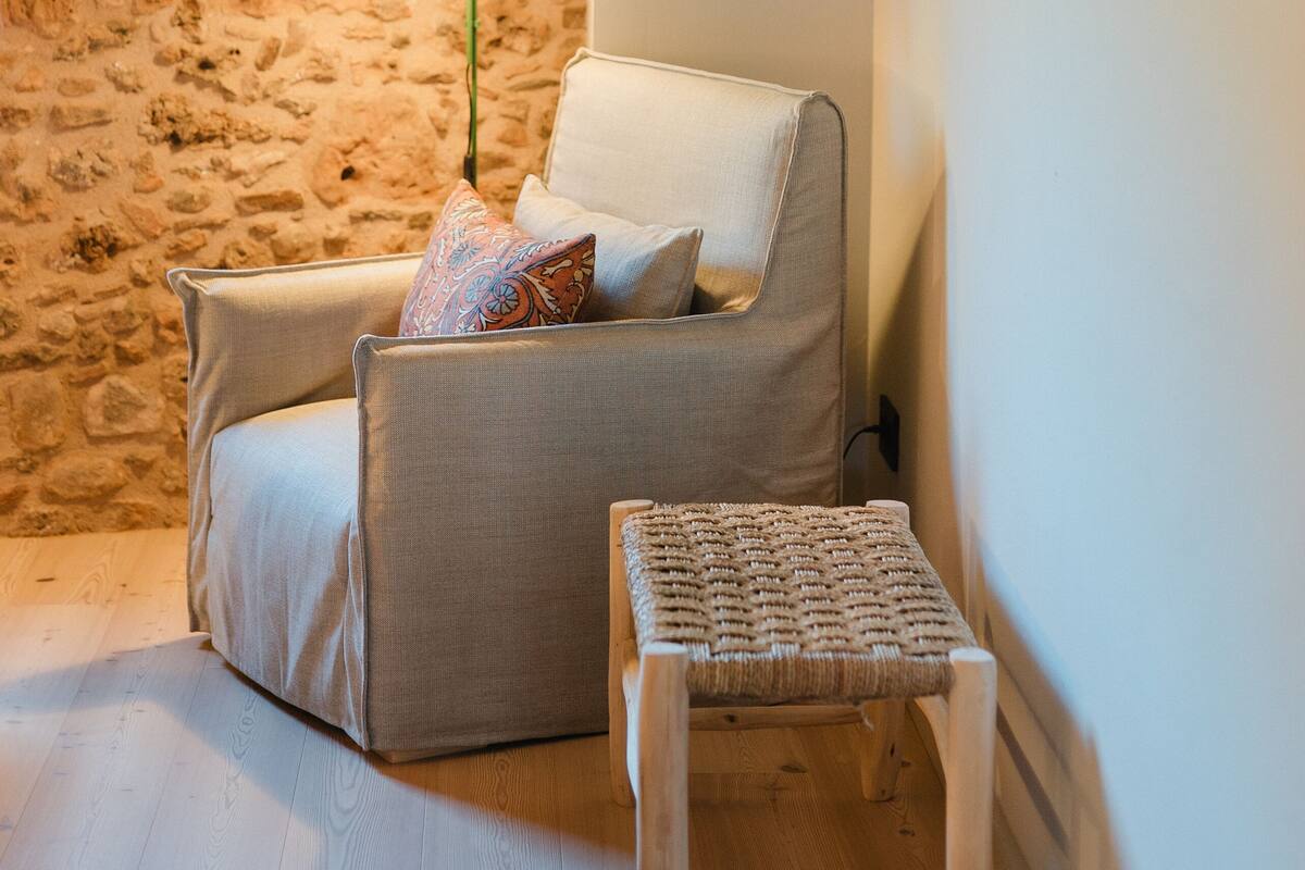 A cozy room with a stone wall, a white armchair, a small wooden table, and a green floor lamp.