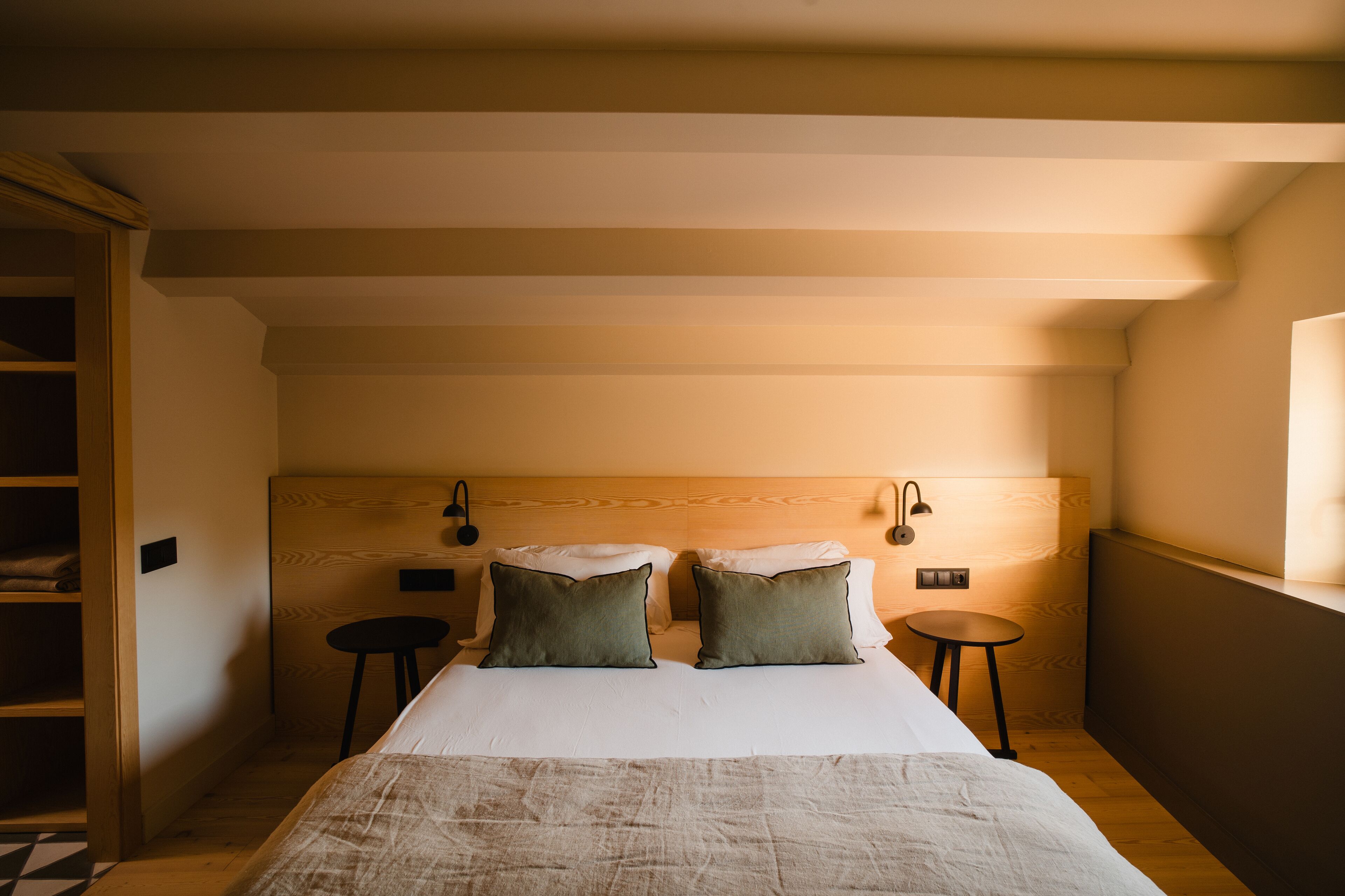 Un dormitorio con una cama grande, dos mesitas de noche, un cabecero de madera y un taburete pequeño.