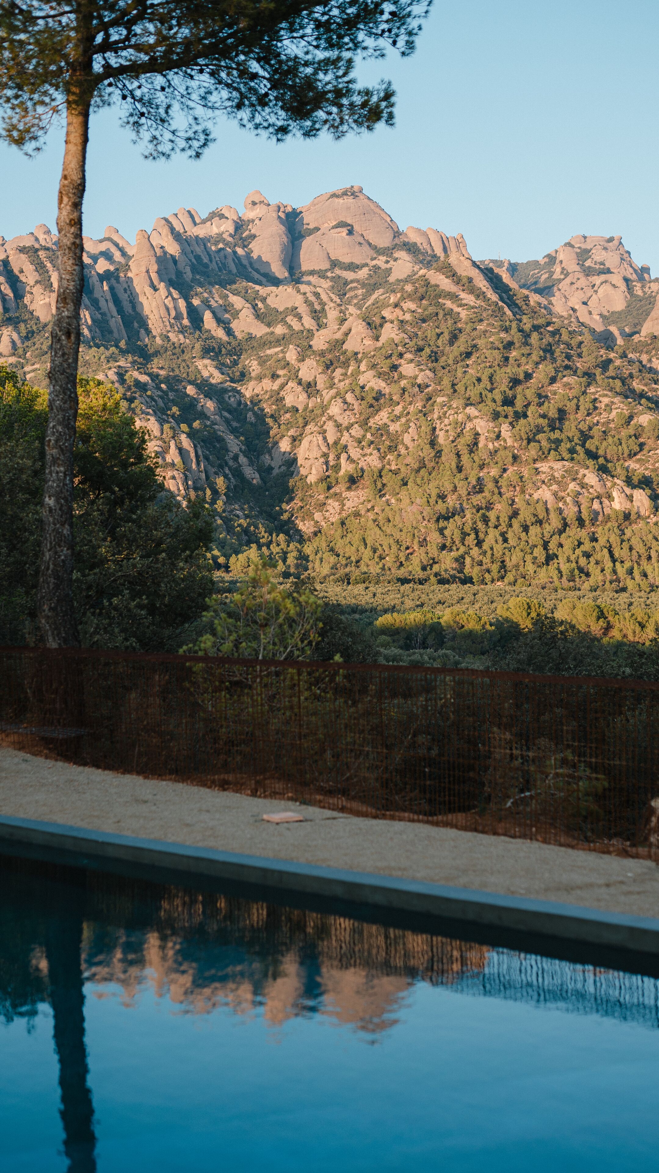 A pool with a mountain backdrop, surrounded by trees and a fence.