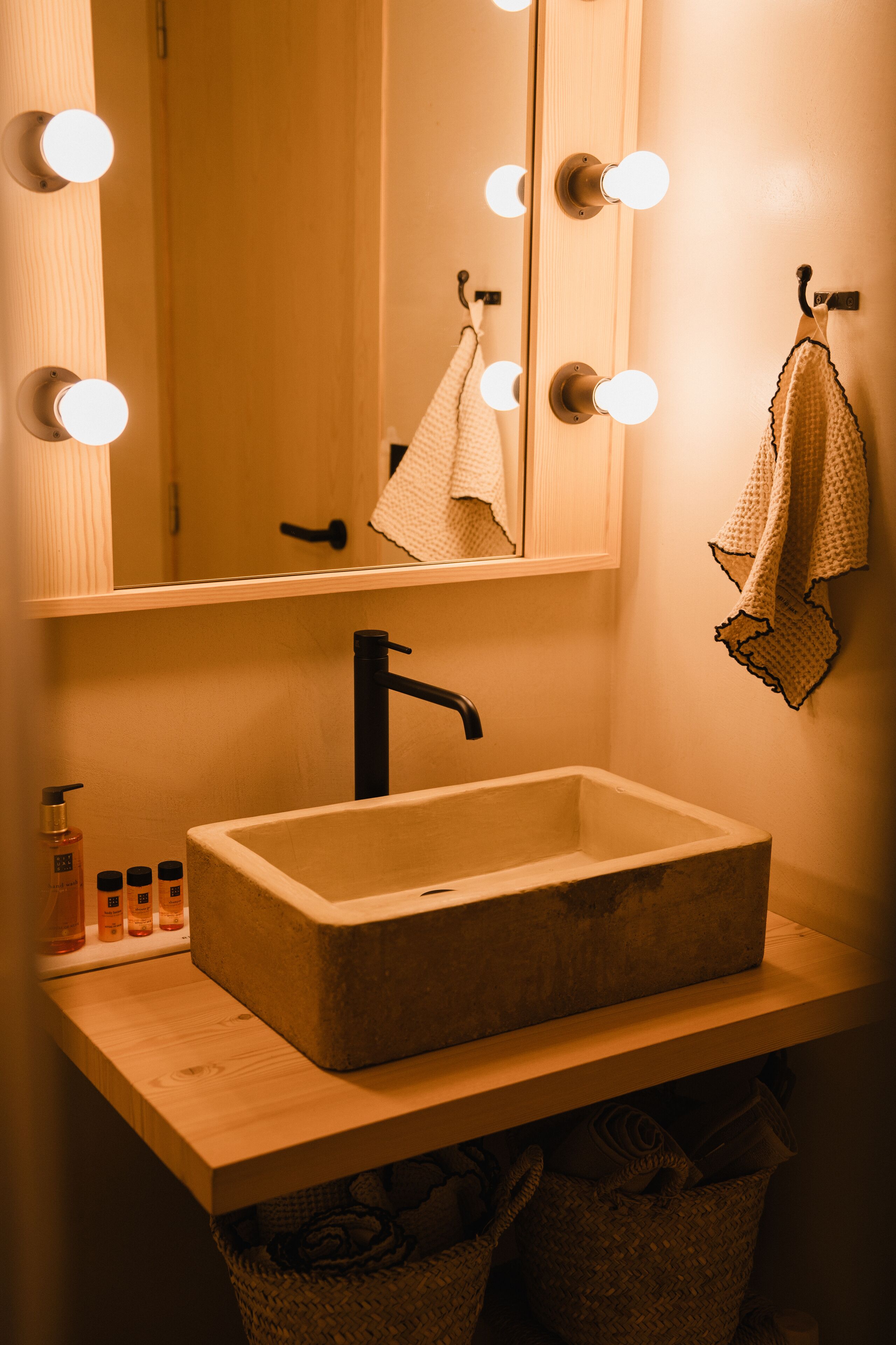 Un baño con un lavamanos rectangular, un espejo con iluminación y toallas colgadas en ganchos.