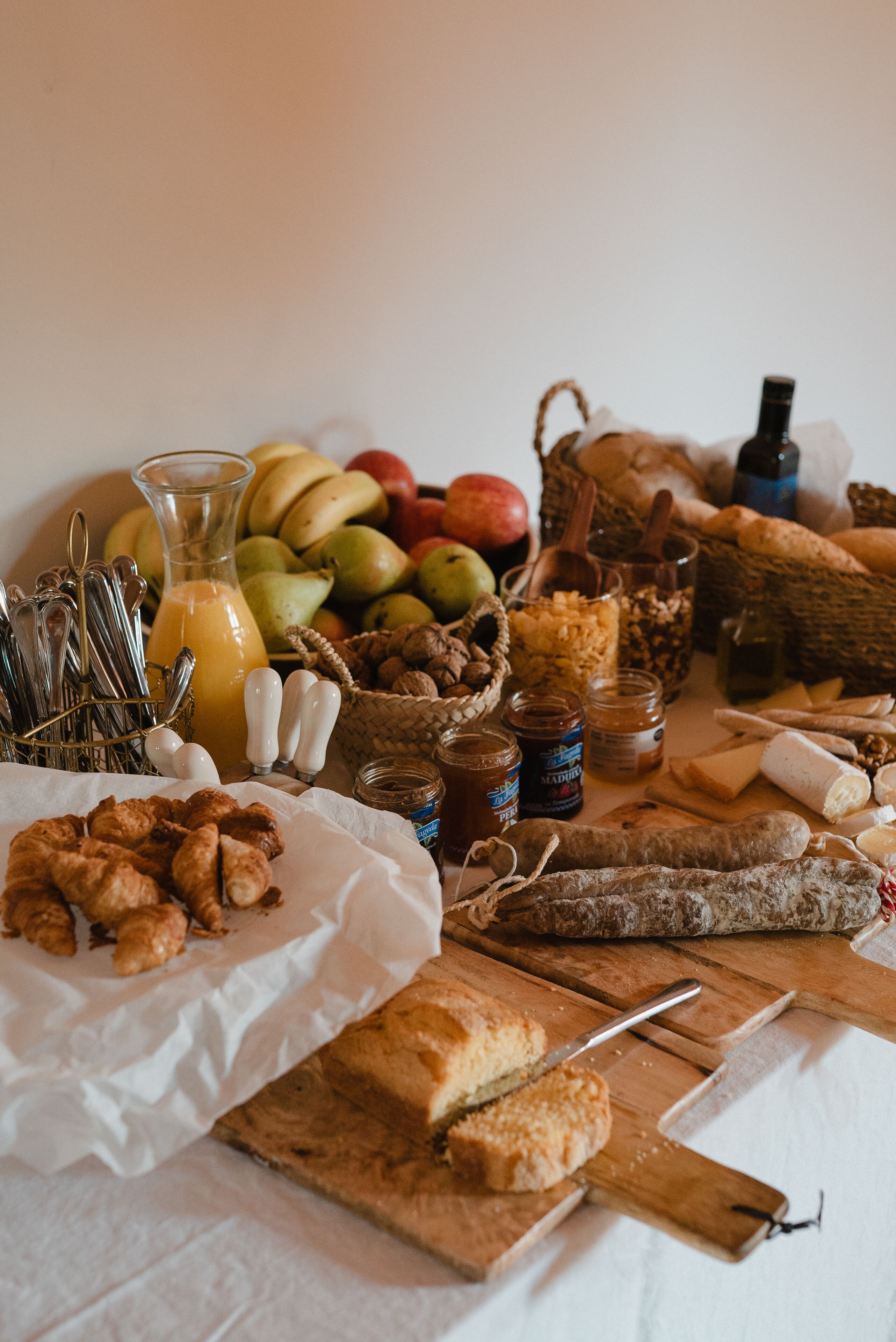 A table with various food items including bread, pastries, fruits, and condiments.