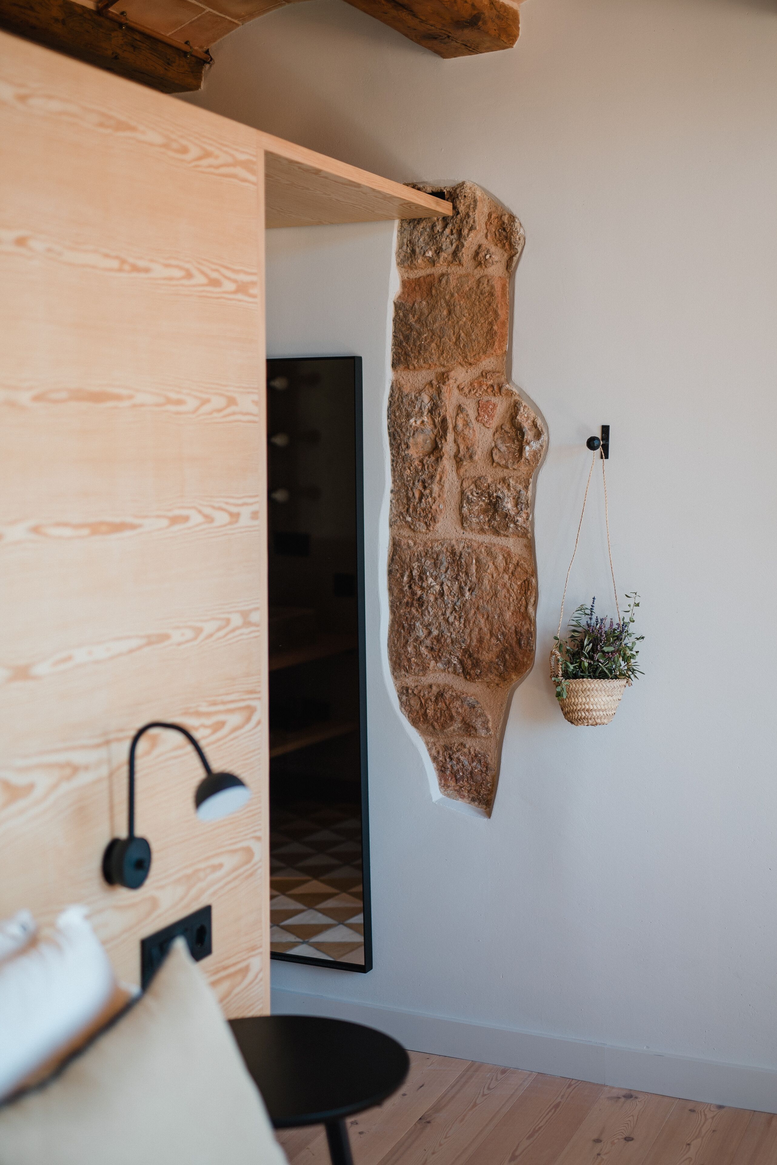 A room with a wooden wall, a stone wall, a hanging plant, and a black lamp.