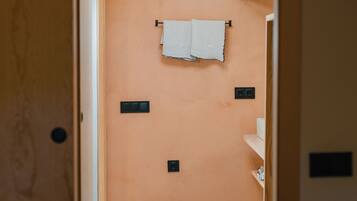 Un pasillo estrecho que conduce a un baño con piso estampado, una toalla colgada en la pared y un estante con objetos.