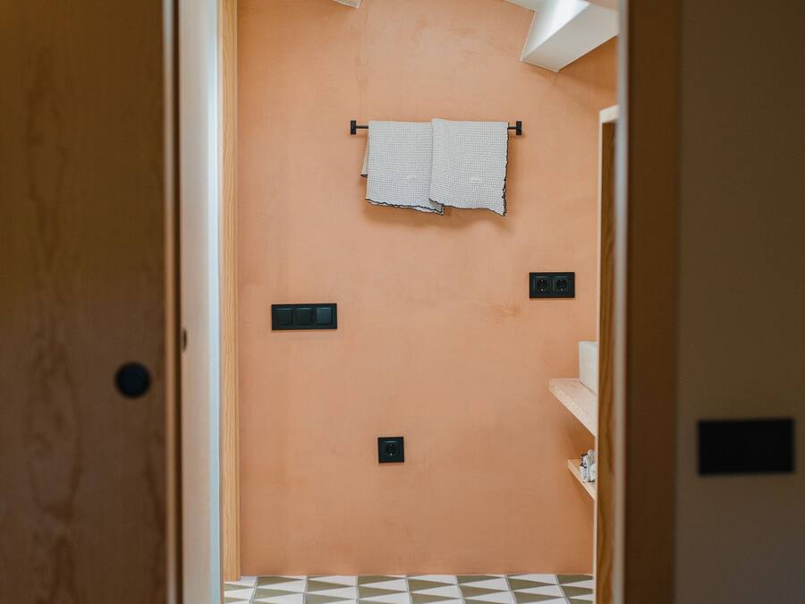 Un pasillo estrecho que conduce a un baño con piso estampado, una toalla colgada en la pared y un estante con objetos.
