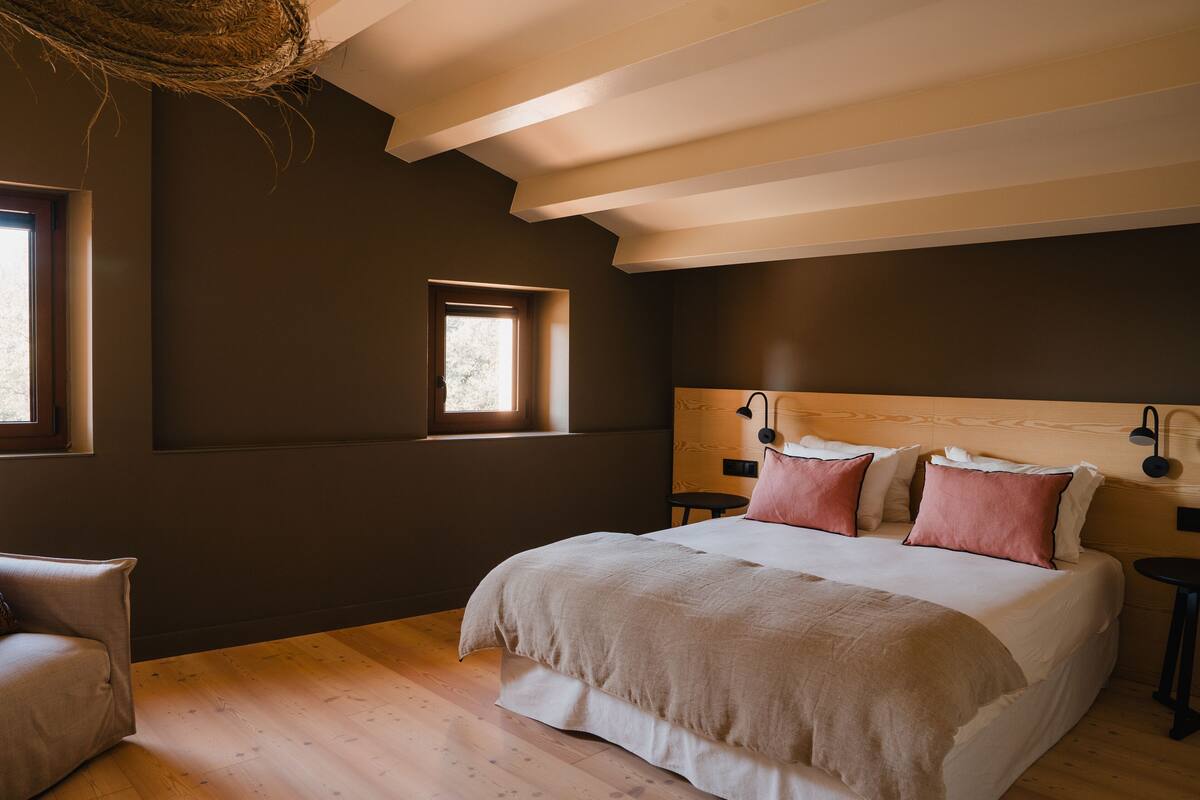 A bedroom with a large bed, a small window, and a wooden ceiling.