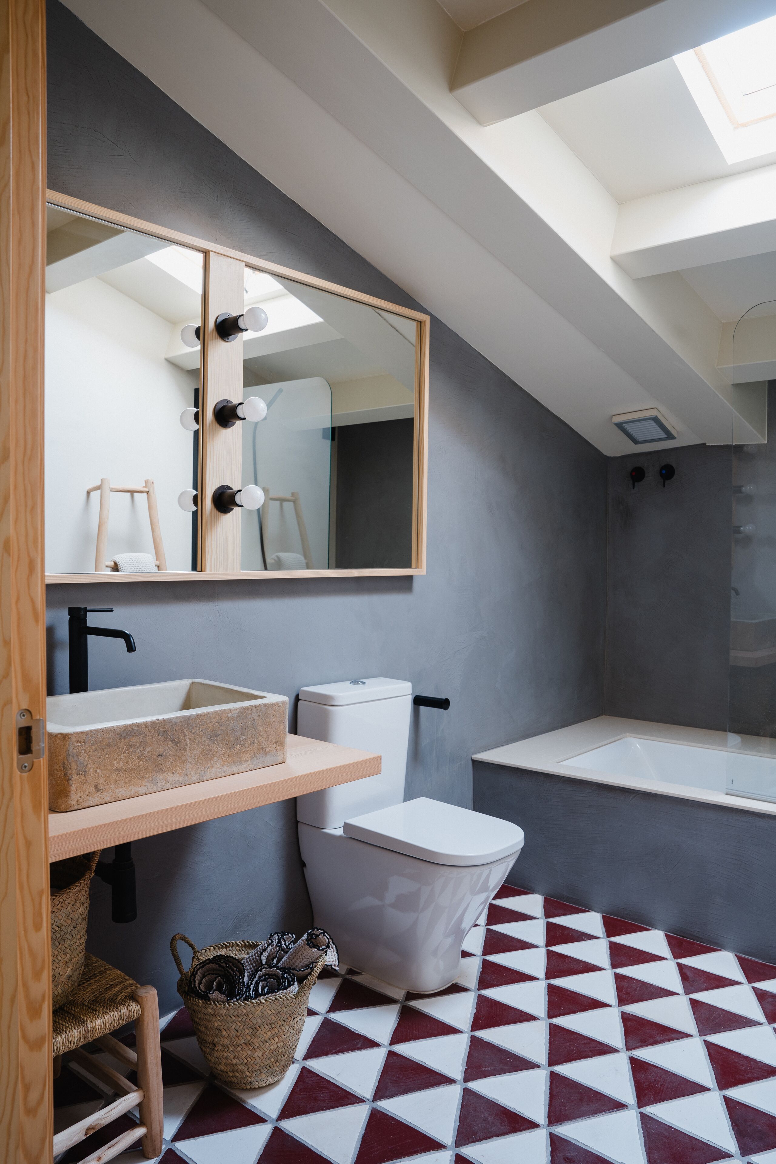 Un baño moderno con tragaluz, un espejo grande, un lavamanos, un inodoro y una bañera.