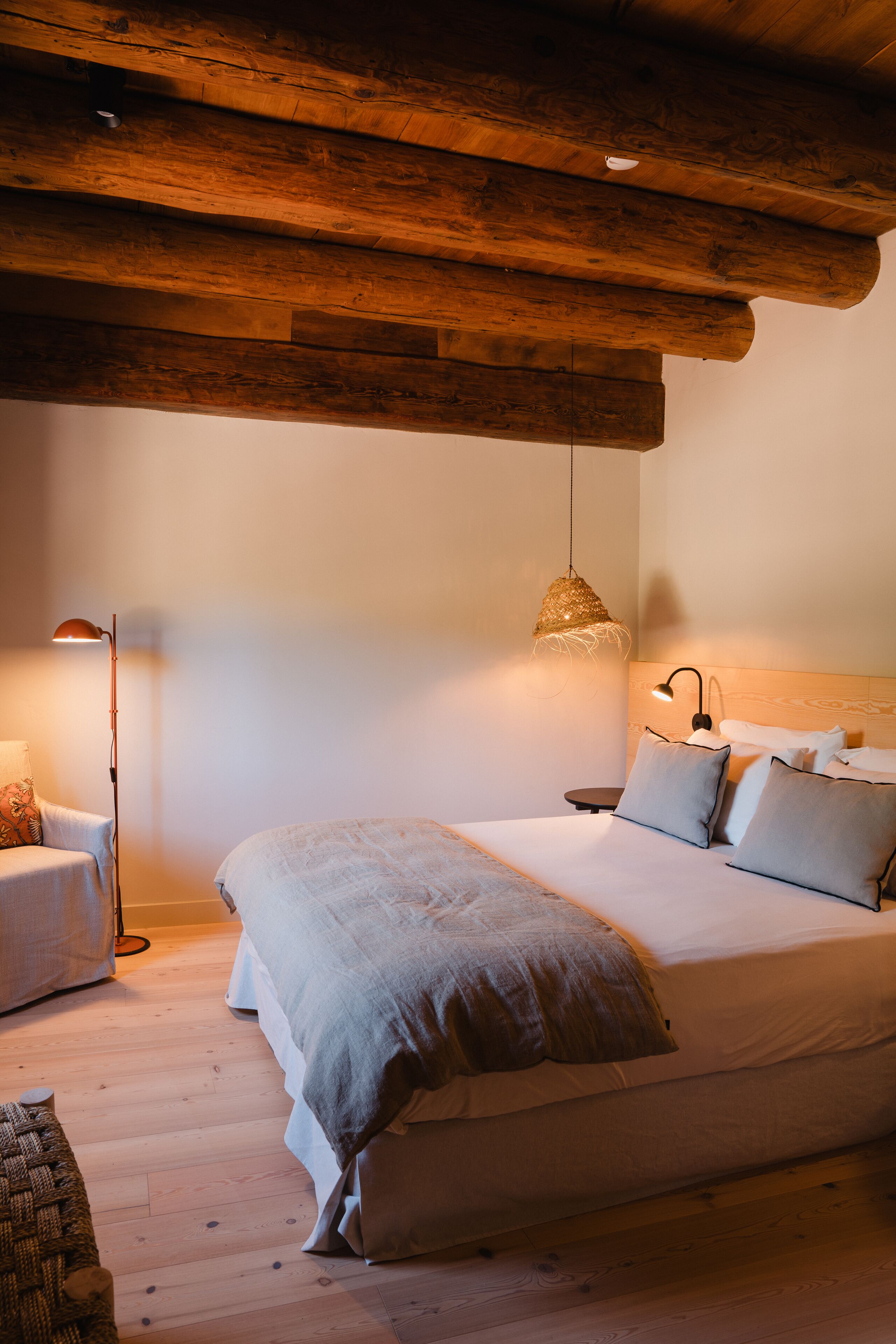 A bedroom with a large bed, a bedside table, a floor lamp, and a hanging light fixture.