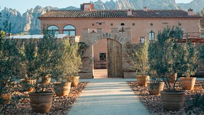 A building with a stone facade, a central archway, and a pathway lined with potted plants. - Hotel Masia Can Farrés (El Bruc)