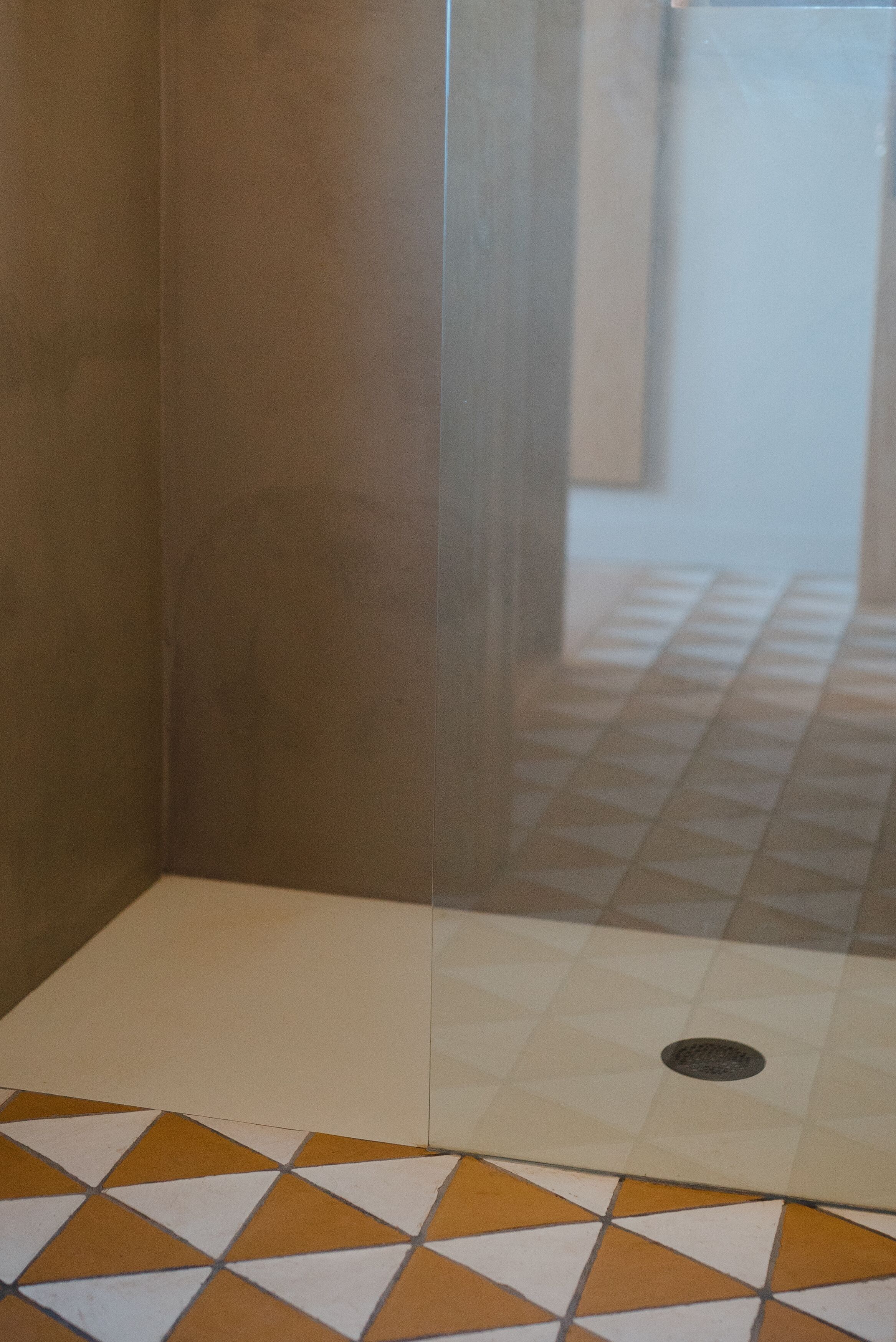 Un área de ducha con azulejos y un patrón geométrico en el suelo, junto a una pared lisa.