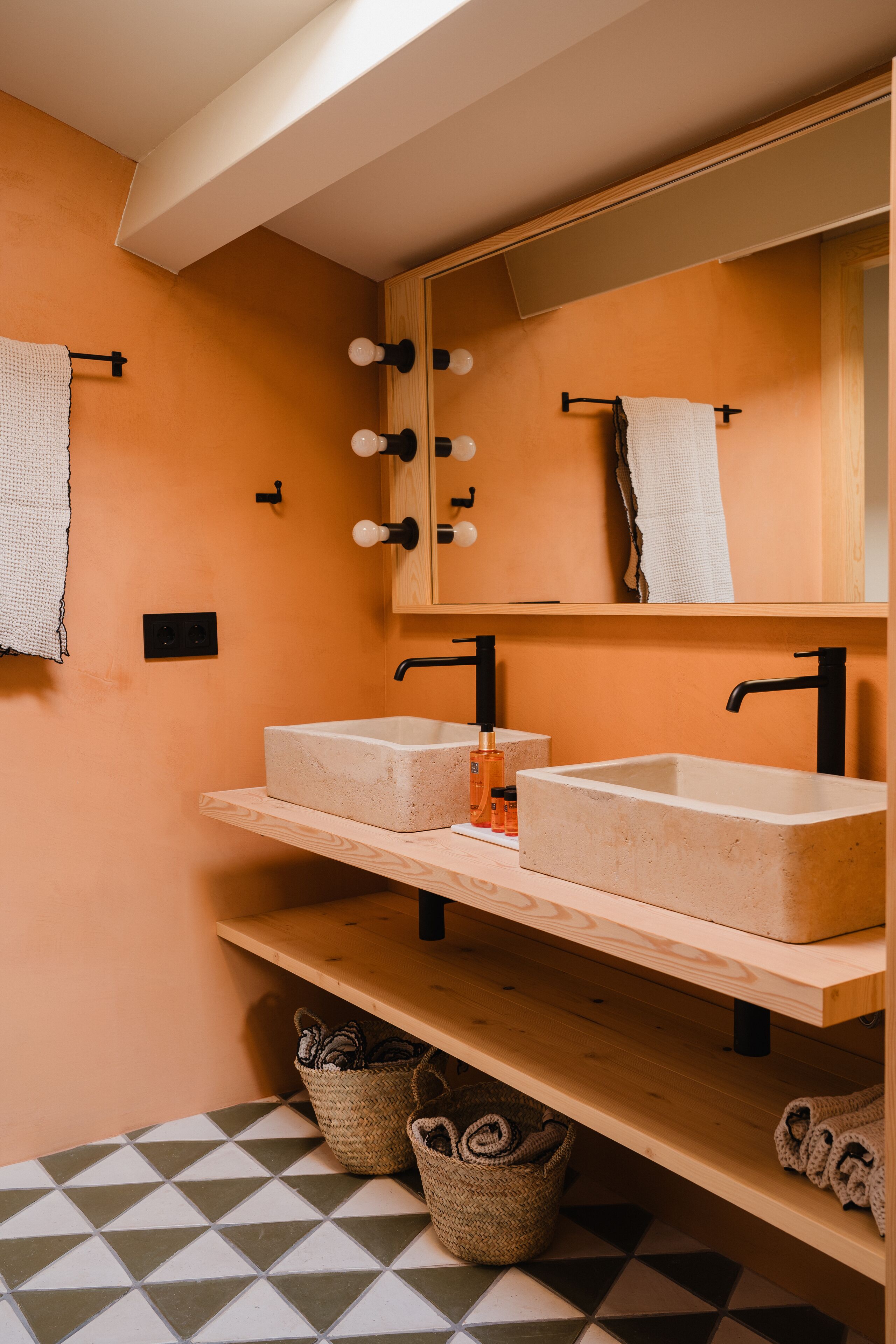 A bathroom with two sinks, a mirror with lights, and a towel rack.
