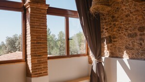 A bedroom with a brick fireplace, large arched windows, and a bed with a gray blanket. - Hotel Masia Can Farrés (El Bruc)