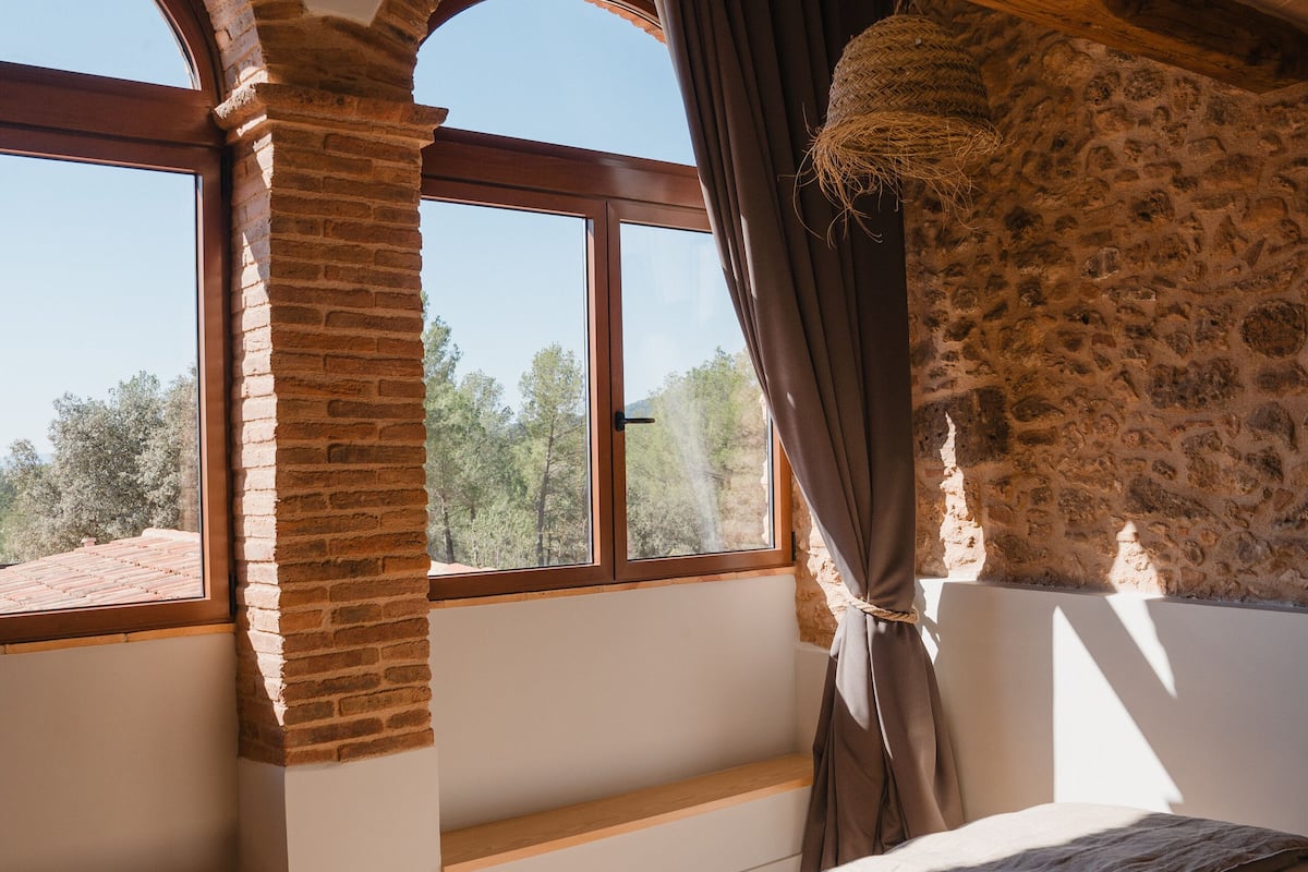 A bedroom with a brick fireplace, large arched windows, and a bed with a gray blanket.