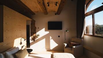 A room with a wooden ceiling, a bed, a chair, a desk, and a large window.