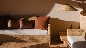 A cozy room with a wooden floor, a sofa with cushions, a hanging light fixture, and a stone wall. - Hotel Masia Can Farrés (El Bruc)