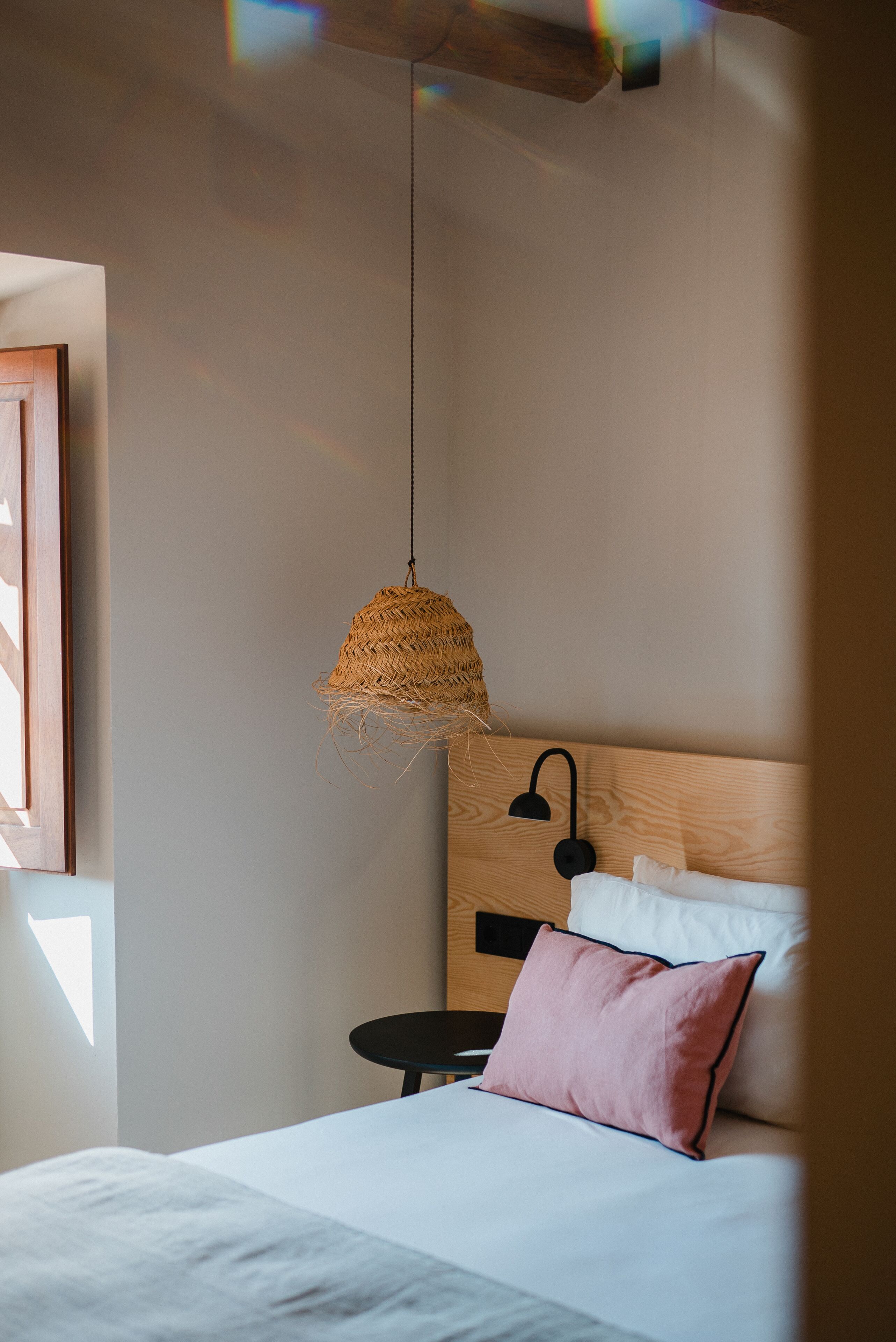 A bedroom with a bed, a hanging woven light fixture, a bedside table, and a nightstand.