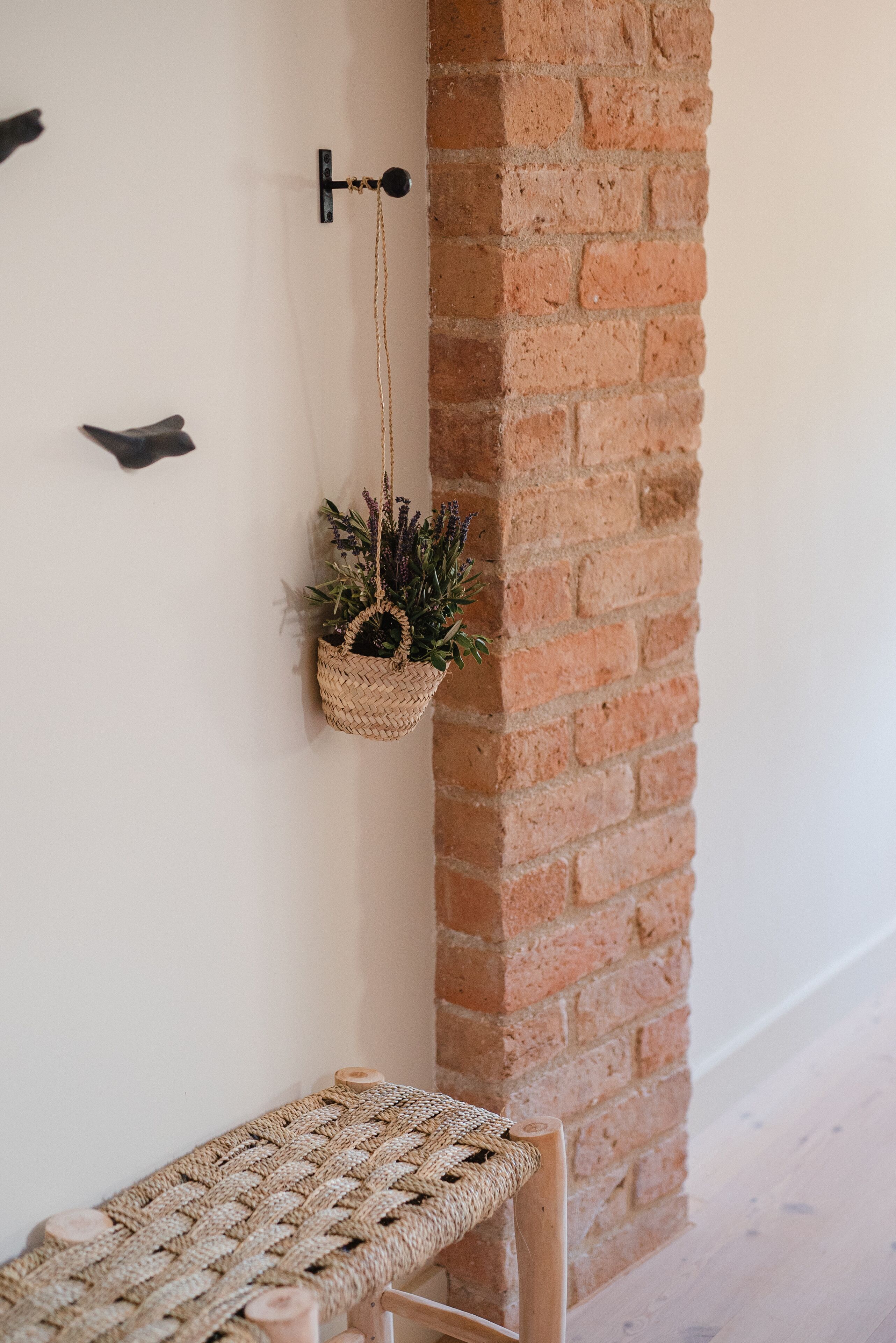 A corner with a woven bench, a hanging plant, and a brick wall.