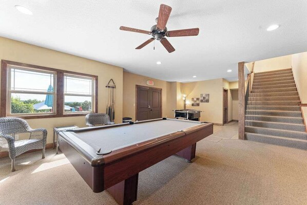 A pool table in a room with a ceiling fan, a staircase, and a door.