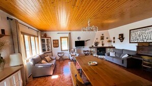 Un salon chaleureux avec un plafond en bois, une table à manger, des canapés et un téléviseur.
