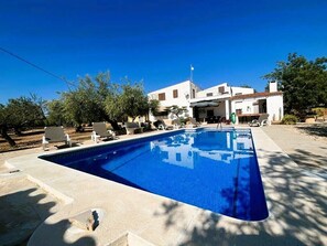 A swimming pool with lounge chairs, a building with a tiled roof, and trees in the background. - Villa Sergi (L'Ametlla de Mar)