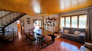 Un vaste espace de vie doté d’un plafond en bois, d’une table à manger avec des bancs, d’un canapé et d’un escalier menant à un autre niveau.