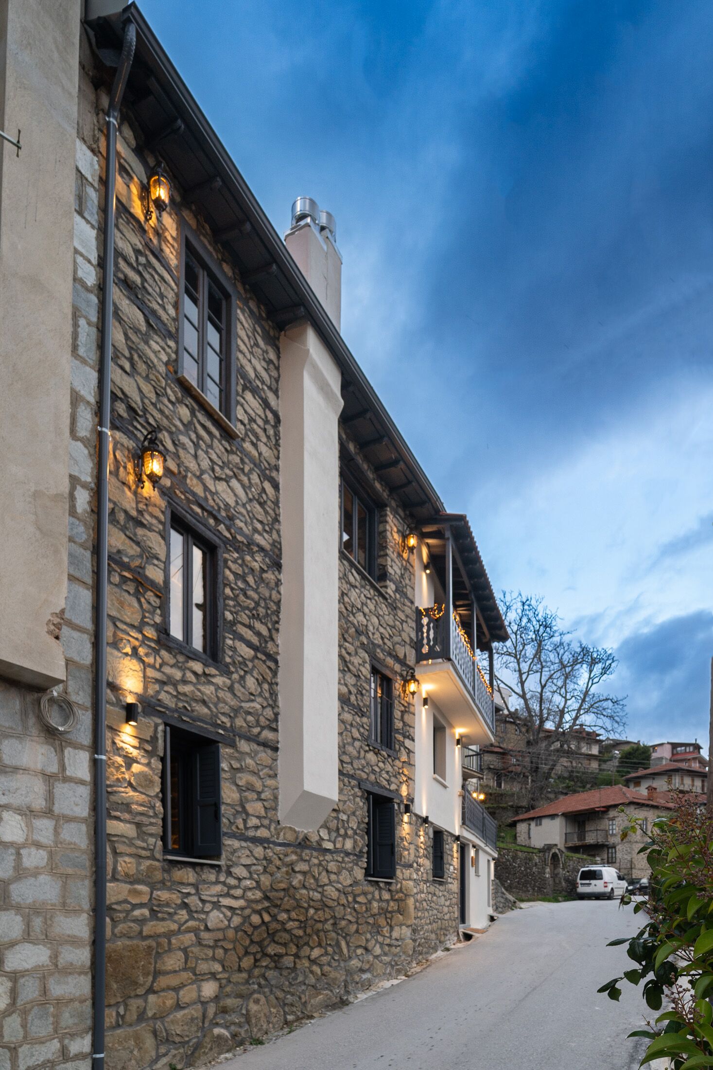 A stone building with multiple windows and balconies, featuring exterior lighting and a narrow street.
