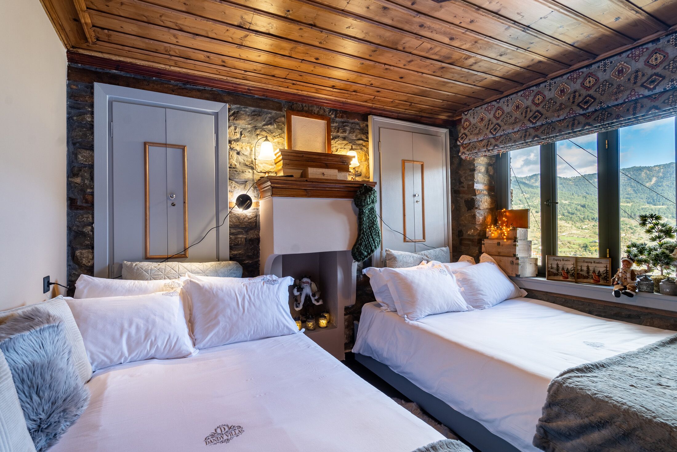 A cozy bedroom with two beds, a stone wall, and a view of the countryside.