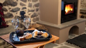 Un plateau contenant des pâtisseries et deux verres d’eau est posé sur une table en bois, devant un mur de pierre et une cheminée où brûle un feu.