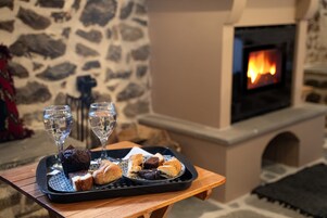 Una bandeja con pasteles y dos vasos de agua sobre una mesa de madera, frente a una pared de piedra y una chimenea encendida.