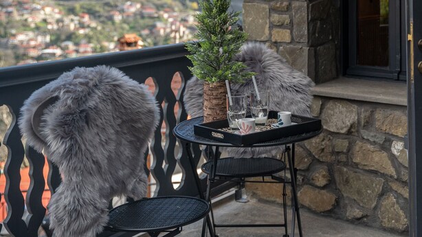 Un balcon avec une table et des chaises, une petite plante en pot, et une vue sur une ville et des montagnes en arrière-plan.