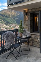 Un balcón con una mesa y sillas, una pequeña planta en maceta y vista a un pueblo y montañas al fondo.