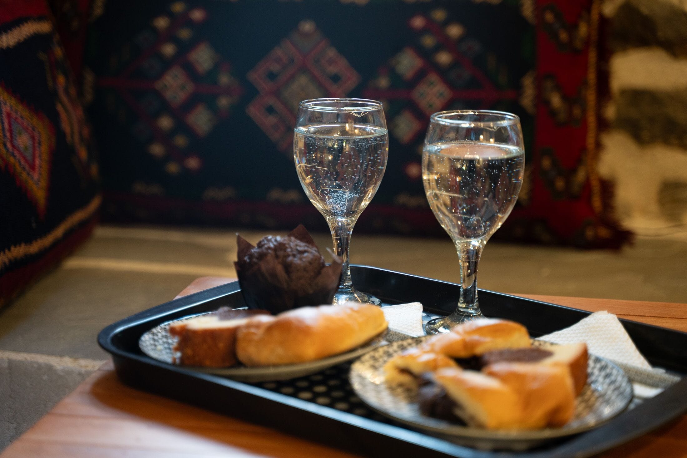 A tray with two glasses of water, a chocolate cake, and several pastries on a table.