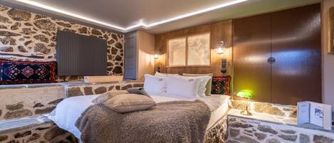 Un dormitorio con pared de piedra, una cama con manta mullida, un armario de madera y un televisor montado.