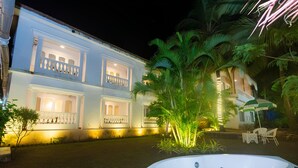A two-story building with balconies, a swimming pool, and a well-lit garden area at night. - Lillywoods NV beach Resort (Calangute)