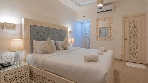 A neatly arranged bedroom with a large bed, bedside lamps, a wall-mounted air conditioner, and a decorative mirror. - Lillywoods NV beach Resort (Calangute)