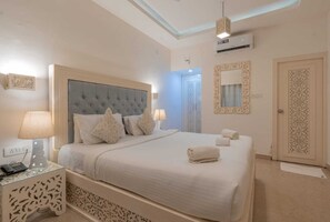 A neatly arranged bedroom with a large bed, bedside lamps, a wall-mounted air conditioner, and a decorative mirror. - Lillywoods NV beach Resort (Calangute)